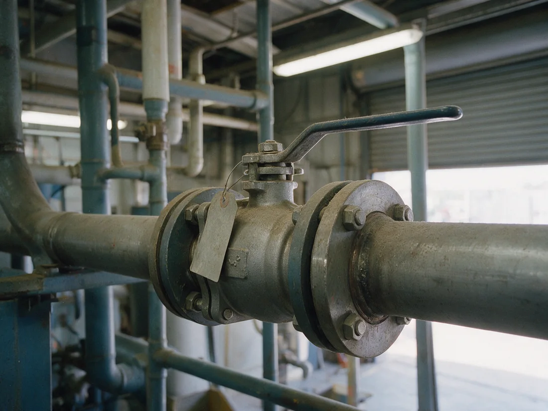 A flanged ball valve bolted into a steel line, lever handle set across the pipe