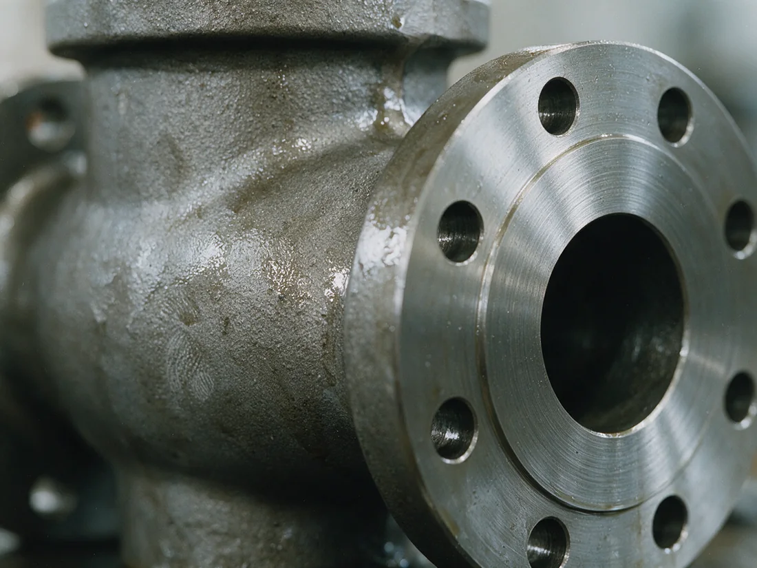 Close-up of a carbon-steel valve casting: a rough sand-cast surface meeting a bright machined flange face