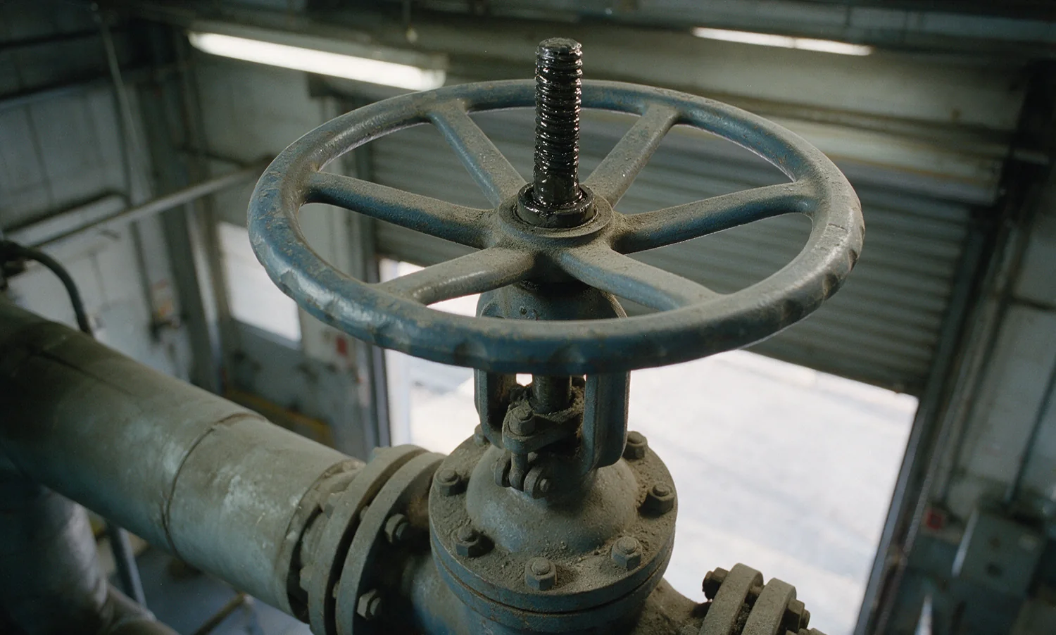 A large spoked handwheel on a flanged pipeline valve, its paint chipped and the rising stem greased